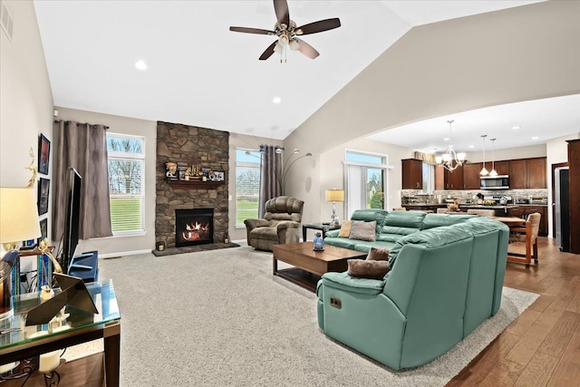 living room with ceiling fan with notable chandelier, a healthy amount of sunlight, a stone fireplace, and wood-type flooring