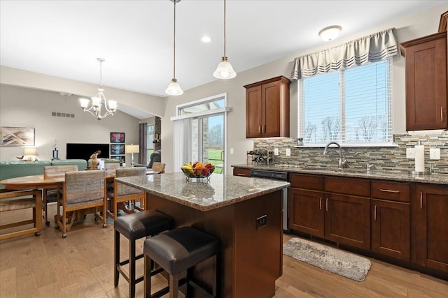 kitchen with a center island, backsplash, light stone countertops, decorative light fixtures, and light hardwood / wood-style floors