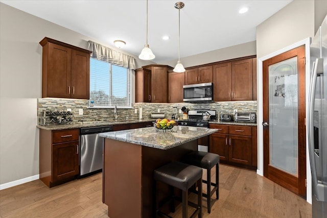 kitchen with appliances with stainless steel finishes, light wood-type flooring, backsplash, light stone counters, and a kitchen island