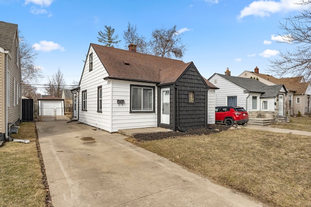 view of front of home featuring an outbuilding, driveway, a front lawn, a shingled roof, and a garage