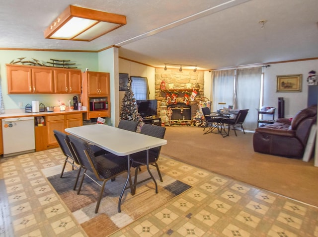 dining space with a stone fireplace, crown molding, and track lighting