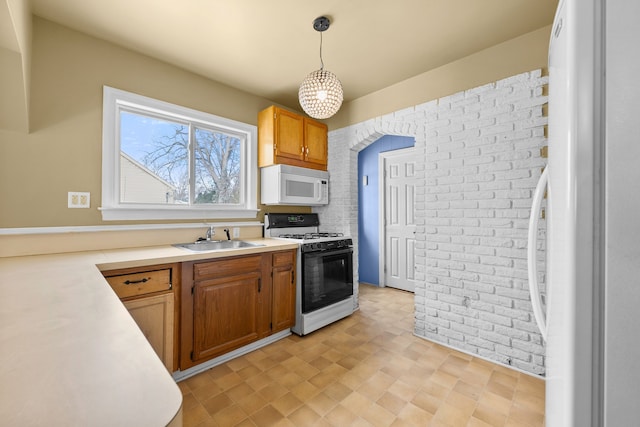 kitchen featuring decorative light fixtures, white appliances, sink, and brick wall