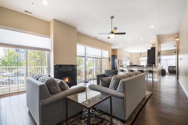 living room with a wealth of natural light, ceiling fan, and dark wood-type flooring