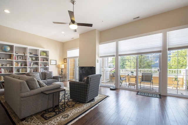 living room featuring a tile fireplace, ceiling fan, and dark wood-type flooring