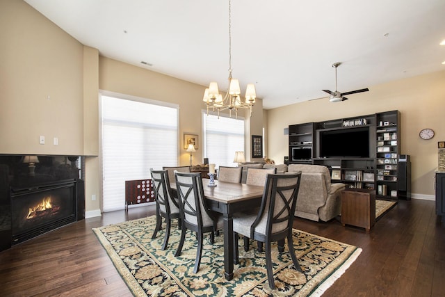 dining space with ceiling fan with notable chandelier, dark hardwood / wood-style flooring, and a fireplace