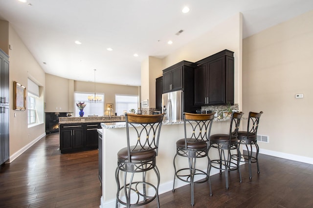 kitchen with a kitchen bar, stainless steel refrigerator with ice dispenser, dark hardwood / wood-style flooring, light stone counters, and pendant lighting