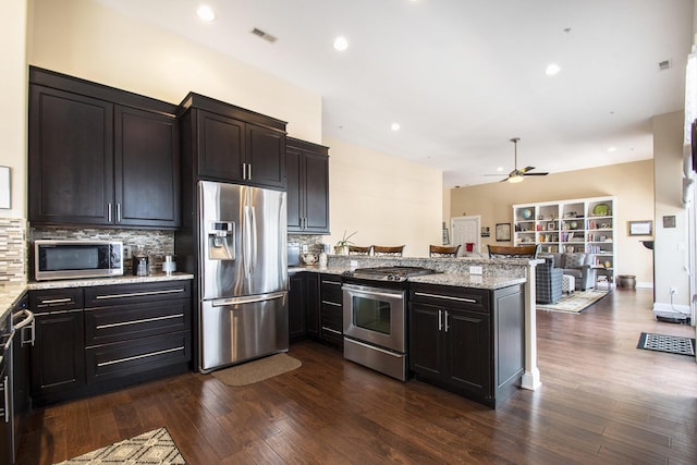 kitchen with dark wood-type flooring, decorative backsplash, light stone countertops, kitchen peninsula, and stainless steel appliances