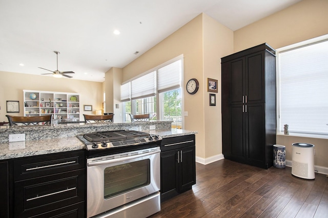 kitchen with stainless steel gas range oven, light stone countertops, ceiling fan, and dark wood-type flooring