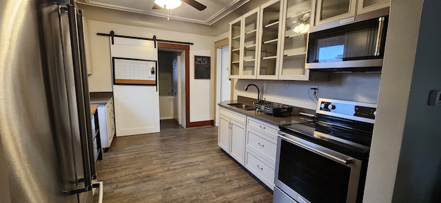 kitchen with a sink, dark countertops, a barn door, appliances with stainless steel finishes, and dark wood-style flooring