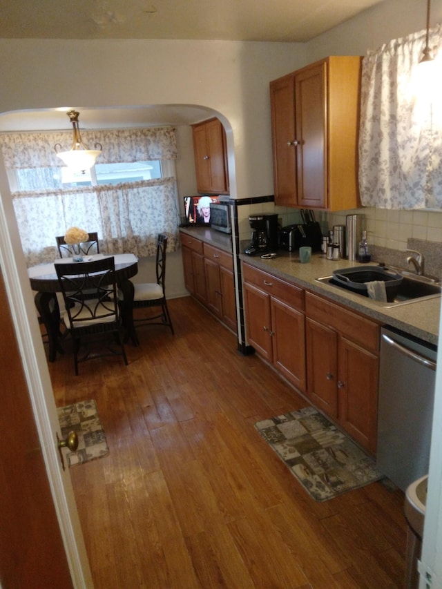 kitchen with sink, stainless steel dishwasher, tasteful backsplash, decorative light fixtures, and wood-type flooring