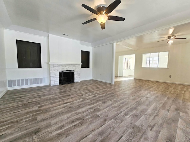 unfurnished living room featuring hardwood / wood-style floors, a stone fireplace, and ceiling fan