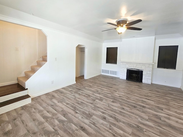 unfurnished living room with a stone fireplace, ceiling fan, and light wood-type flooring