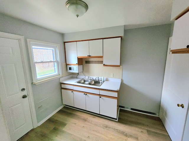 kitchen with white cabinets, decorative backsplash, light hardwood / wood-style floors, and sink