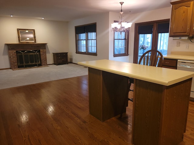 kitchen with a breakfast bar, pendant lighting, dishwasher, a brick fireplace, and dark wood-type flooring