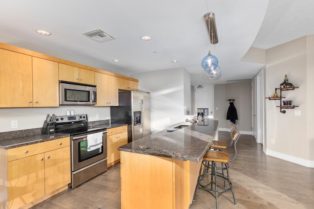335 Bridge St NW Unit 2602, Grand Rapids, MI 49504 - kitchen featuring appliances with stainless steel finishes, light brown cabinets, wood finished floors, a breakfast bar area, and dark stone countertops
