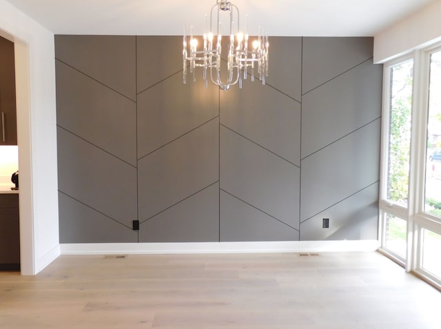 unfurnished dining area with a notable chandelier and light wood-type flooring