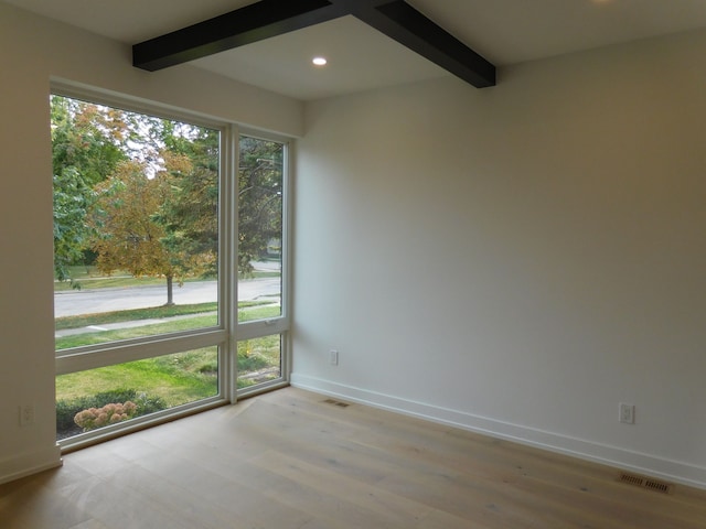 spare room with a healthy amount of sunlight, light hardwood / wood-style floors, and beam ceiling