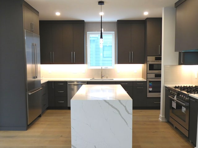 kitchen featuring sink, appliances with stainless steel finishes, decorative light fixtures, light hardwood / wood-style floors, and light stone counters