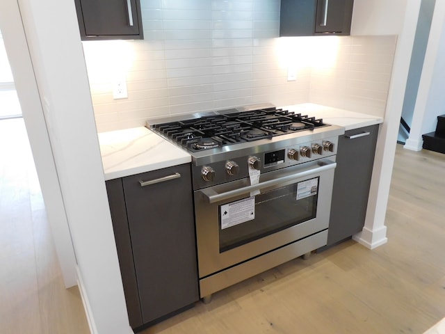 kitchen featuring light stone countertops, light hardwood / wood-style flooring, luxury stove, decorative backsplash, and dark brown cabinets