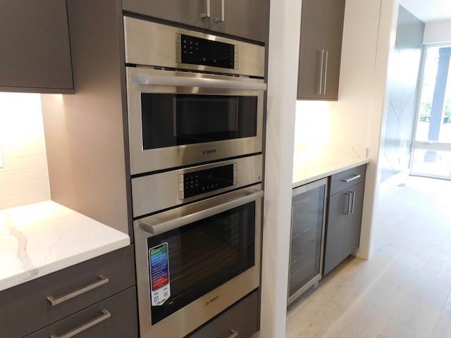 kitchen with light stone countertops, light wood-type flooring, double oven, and beverage cooler