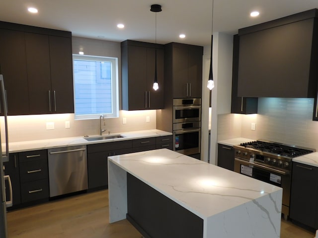 kitchen with light wood-type flooring, stainless steel appliances, sink, a center island, and hanging light fixtures