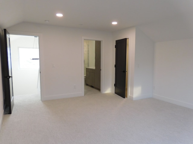 interior space featuring ensuite bathroom, light colored carpet, and vaulted ceiling