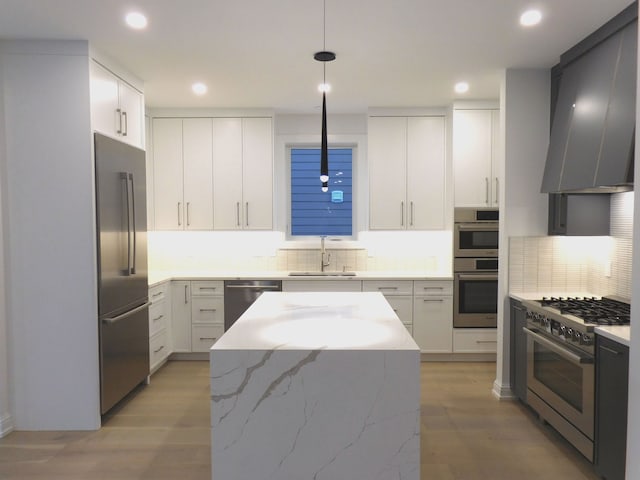 kitchen featuring decorative backsplash, wall chimney exhaust hood, appliances with stainless steel finishes, light stone countertops, and a sink