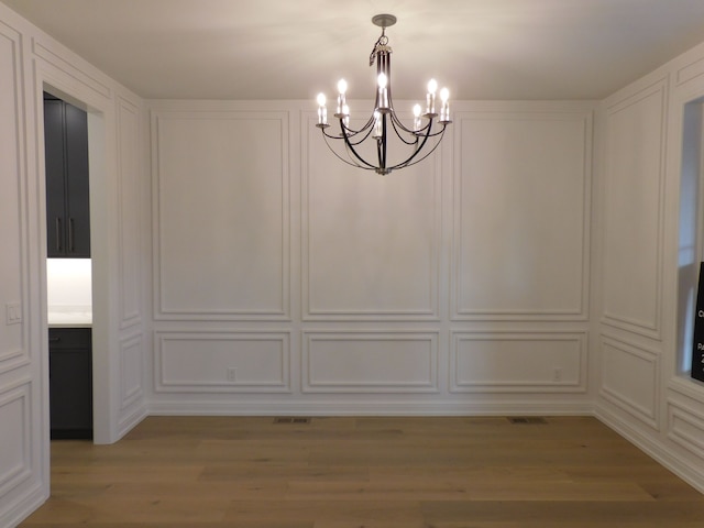 unfurnished dining area featuring a chandelier, light wood-type flooring, and a decorative wall