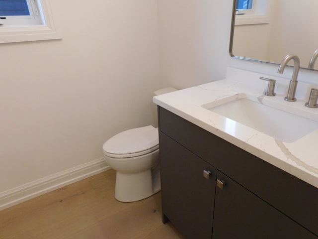 half bathroom with toilet, wood finished floors, vanity, and baseboards