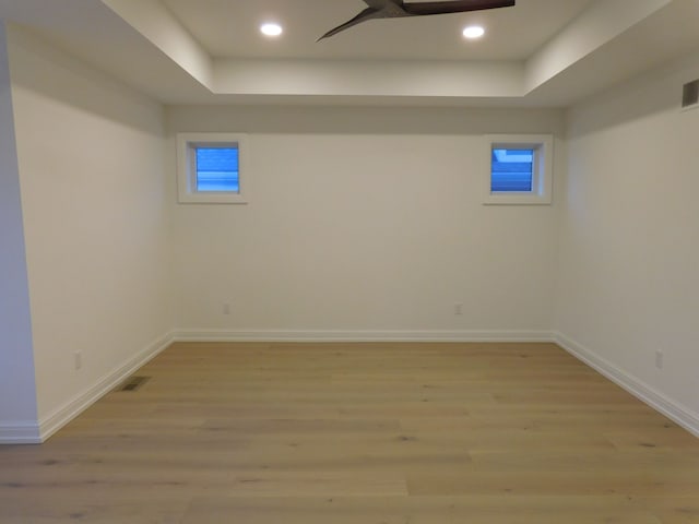 basement featuring light wood-style floors, baseboards, visible vents, and a ceiling fan