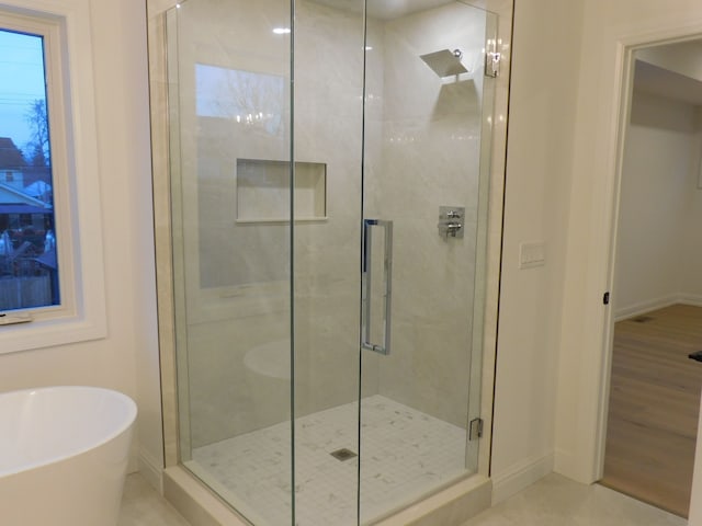 bathroom with a soaking tub, a shower stall, and baseboards