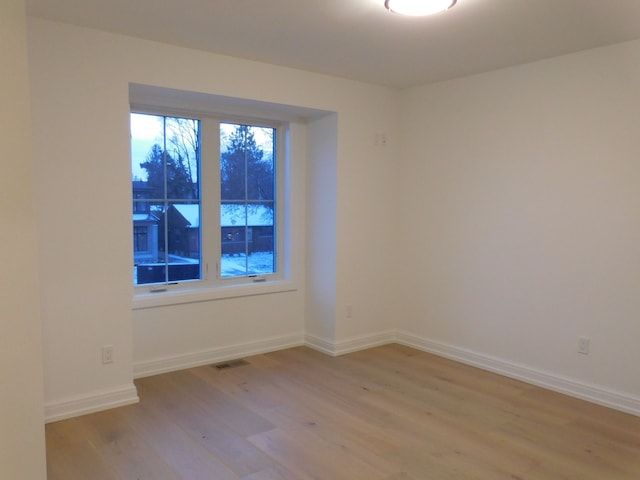 empty room featuring light wood-style flooring, visible vents, and baseboards