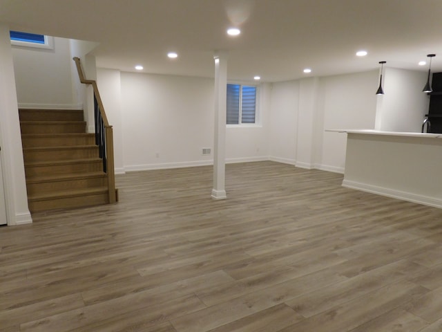 finished below grade area featuring stairs, light wood finished floors, baseboards, and recessed lighting