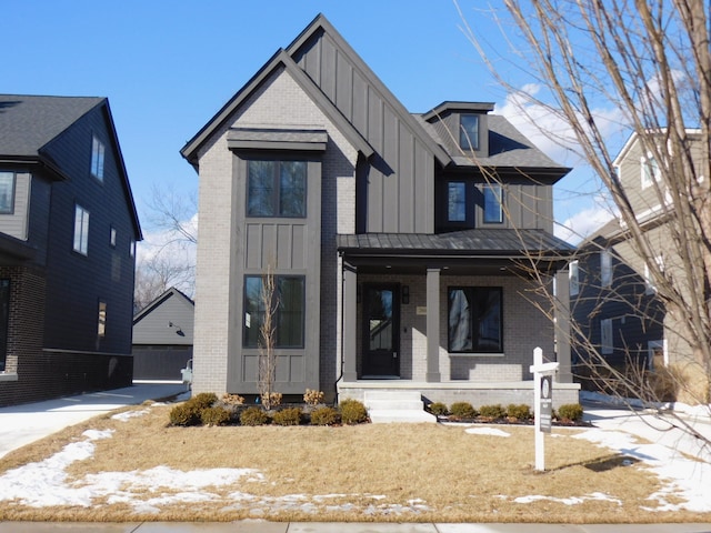 view of front facade featuring an outbuilding, a standing seam roof, a porch, brick siding, and board and batten siding