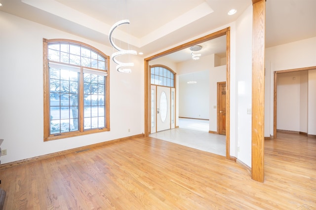 unfurnished room featuring an inviting chandelier, light hardwood / wood-style flooring, and a raised ceiling