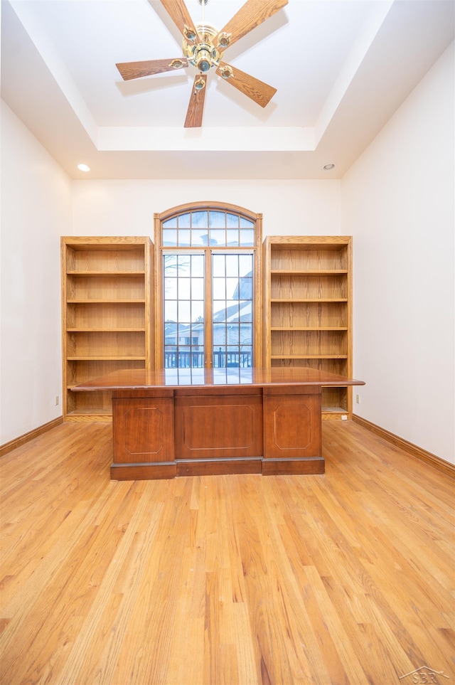 unfurnished office featuring ceiling fan, light wood-type flooring, and a tray ceiling