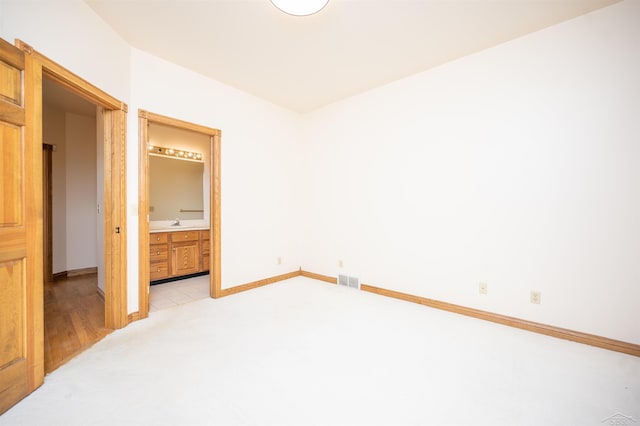 unfurnished bedroom featuring light carpet, ensuite bath, and sink