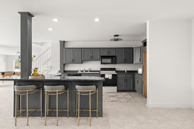 kitchen with dark stone counters, white electric range, sink, gray cabinets, and a breakfast bar area