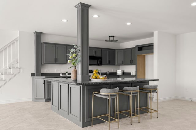 kitchen with gray cabinetry, a center island, decorative columns, dark stone countertops, and a kitchen bar