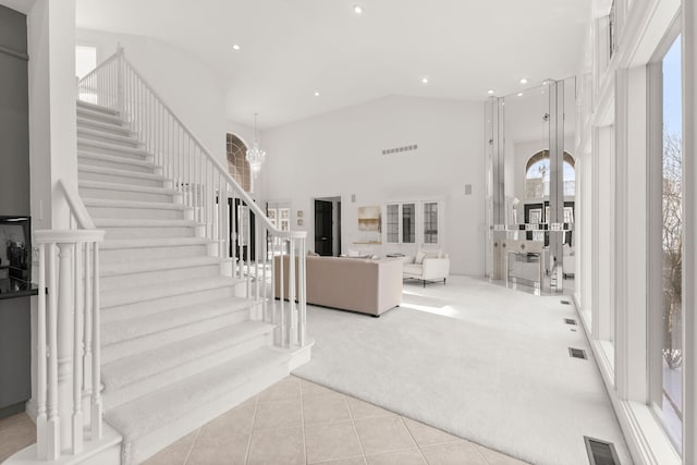 entryway featuring light colored carpet, high vaulted ceiling, and a notable chandelier