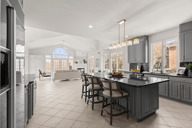 kitchen with gray cabinetry, a breakfast bar, a center island, sink, and vaulted ceiling