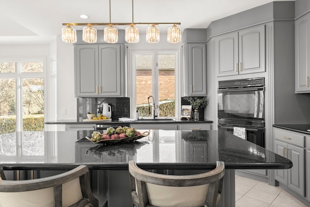 kitchen with backsplash, dark stone counters, black double oven, gray cabinets, and light tile patterned floors