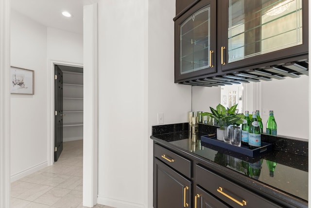 bar featuring dark brown cabinets, light tile patterned floors, and dark stone countertops