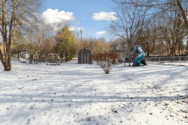 snowy yard with a storage shed and a playground