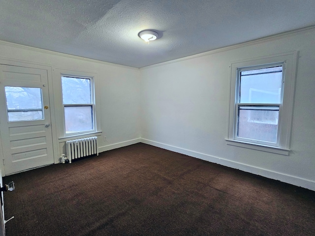 spare room with dark colored carpet, crown molding, a textured ceiling, and radiator