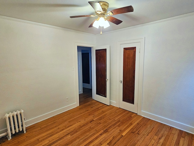 unfurnished bedroom with hardwood / wood-style flooring, ceiling fan, radiator heating unit, and crown molding