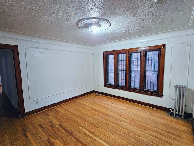 unfurnished room with light hardwood / wood-style floors, radiator heating unit, and a textured ceiling