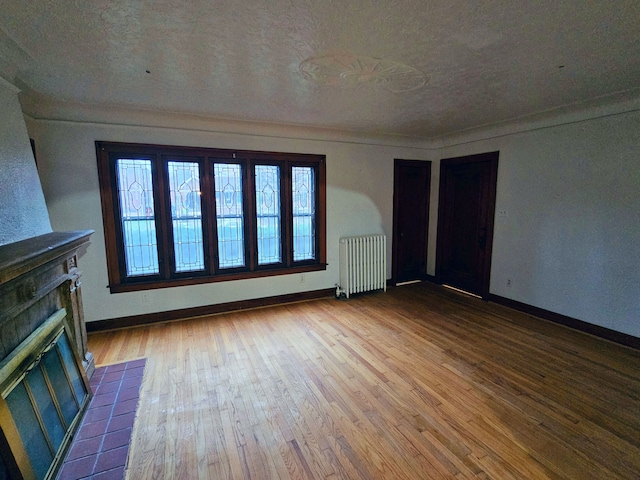 unfurnished living room with radiator, a fireplace, a textured ceiling, and light wood-type flooring