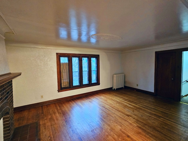 unfurnished living room featuring radiator heating unit, hardwood / wood-style flooring, and a brick fireplace