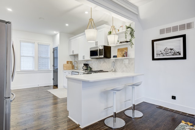 kitchen featuring a kitchen bar, appliances with stainless steel finishes, dark hardwood / wood-style floors, white cabinetry, and hanging light fixtures